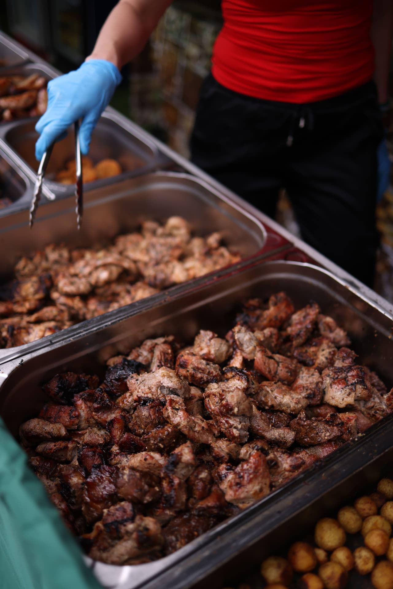 Caterer serving grilled meat from stainless steel bain-marie trays