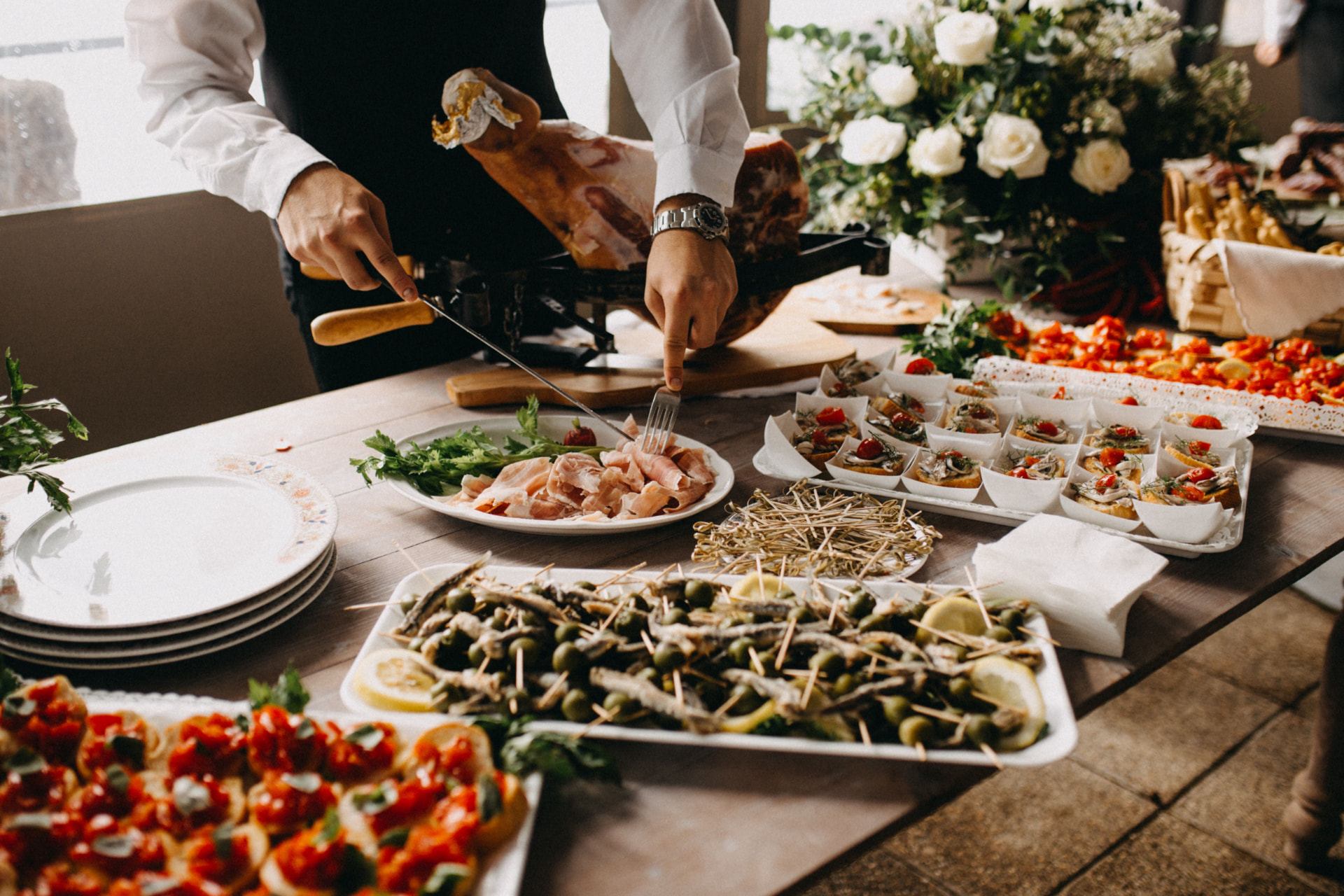 Uniformed server carving cured meat at an event catering station